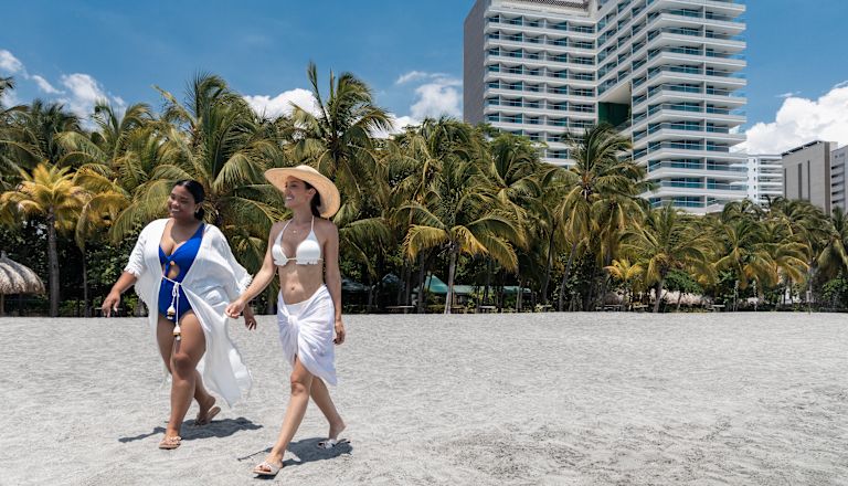 Dos mujeres caminando por la playa, con el hotel de fondo