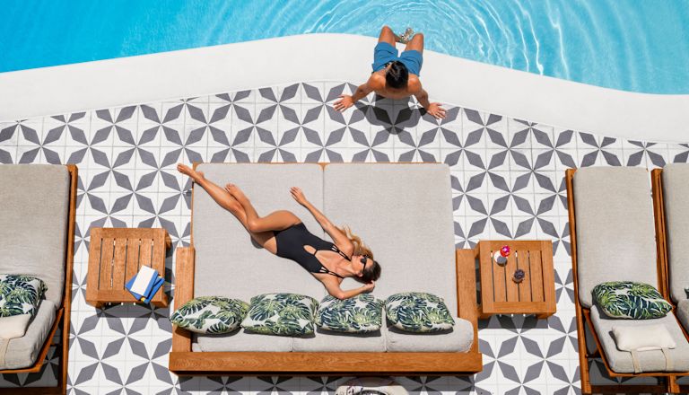 Foto aérea de uma mulher tomando sol na piscina com um homem sentado na piscina