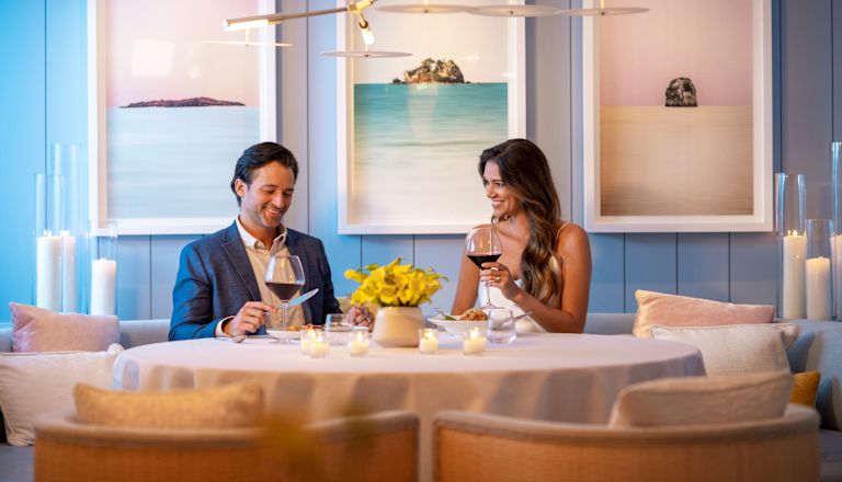 Casal sentado à mesa com pintura atrás deles