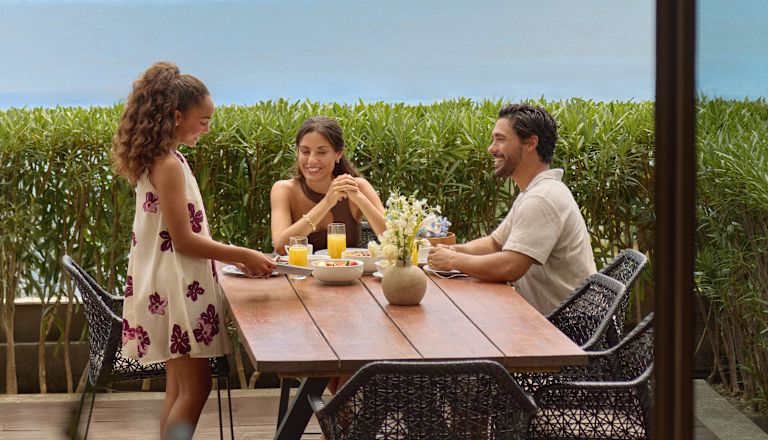 Mother, father and daughter enjoying breakfast on the terrace of their suite