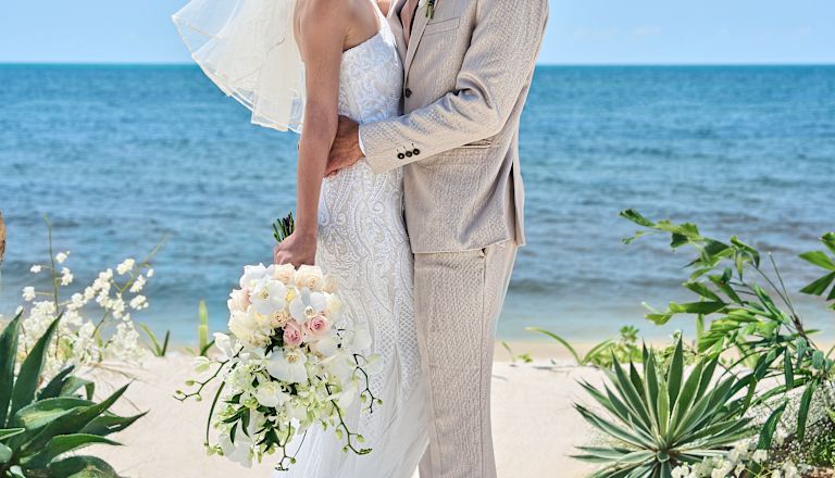 bride & groom standing on the beach hugging