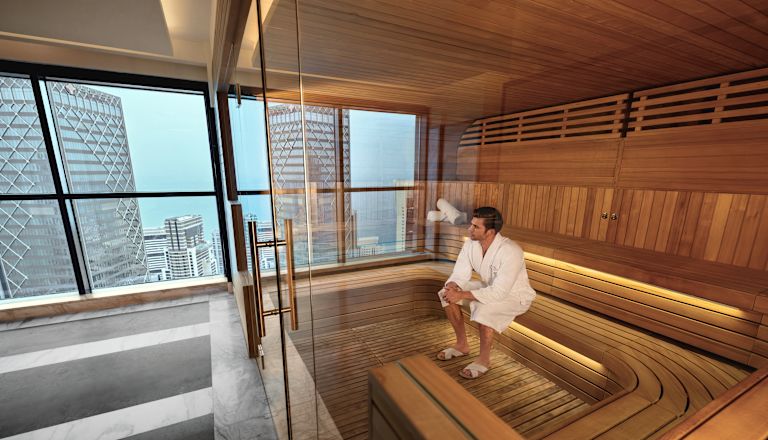Người đàn ông mặc áo choàng trắng đang thư giãn trong phòng xông hơi với tầm nhìn ra thành phố