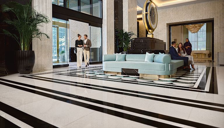 Người đàn ông và phụ nữ bước qua lối vào khách sạn vào khu vực sảnh với đồng hồ