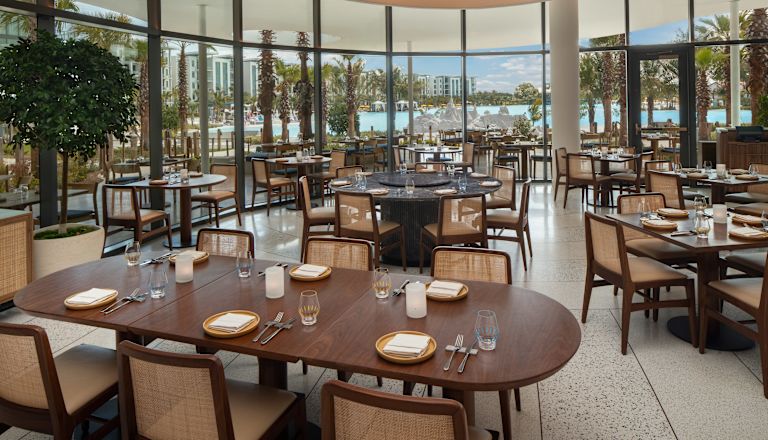Sala de mese a restaurantului Sophias cu ferestre pe toată înălțimea peretelui și apă albastru deschis.