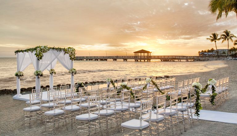 beach wedding ceremony set up, white chairs, gazebo, at sunset