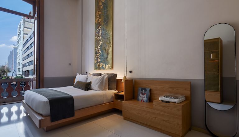 Camera con letto, doppie porte aperte sul balcone e sedile a panca.