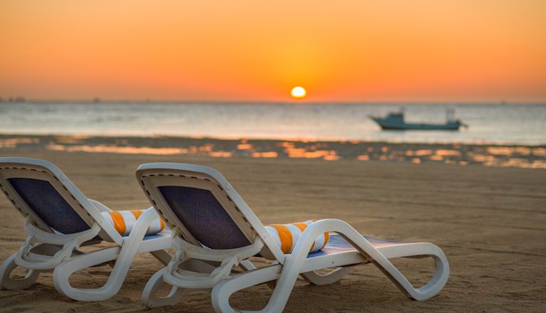 Beach with Deck Chairs and View of Sunrise above Ocean with Boat