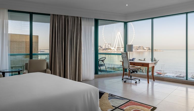 Guest room with bed, work desk and view of ferris wheel