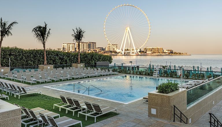 Outdoor pool with surrounding loungers and ferris wheel