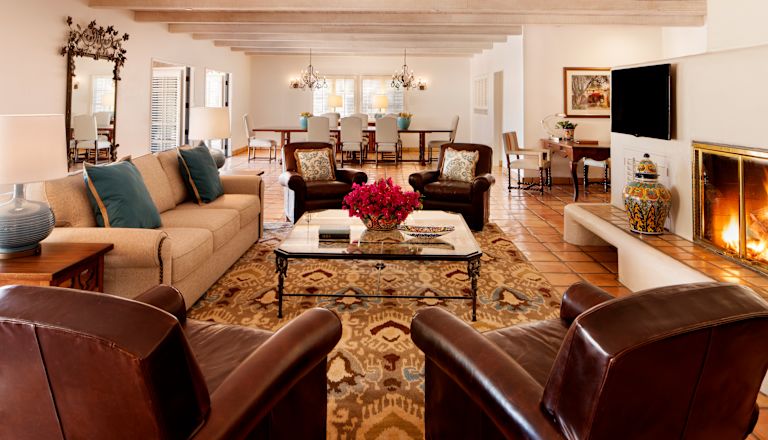 Hacienda Suite living area with ample seating, fire burning in the fireplace, large flatscreen TV, work desk, and dining table with seating for eight