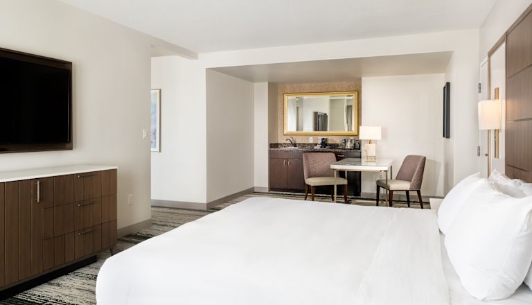 Suite con cama King, televisor, escritorio y área de bar con fregadero