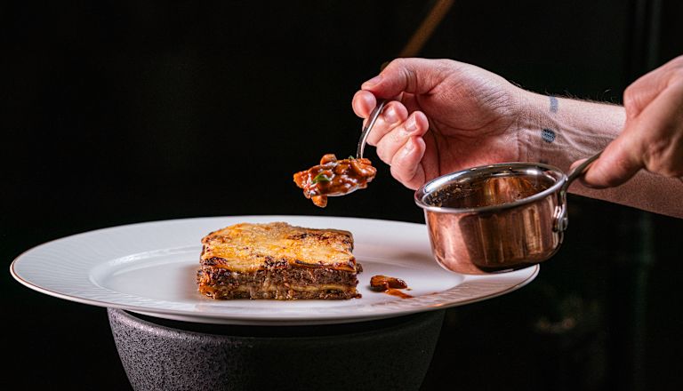 Một bàn tay cầm dĩa với một mảnh Lasagna trên đĩa tại Chợ Tribeca