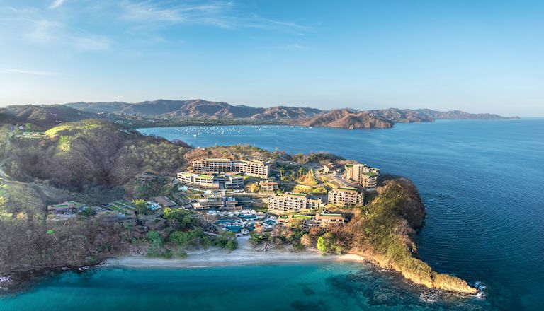 Fotografía en dron de la fachada del hotel desde la distancia, mostrando el océano y la costa circundantes