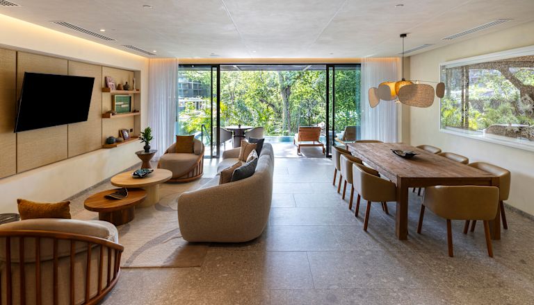 Área de lounge de la suite Pacifico, sofá, televisor, mesa para comer, vista desde la ventana del patio privado y la piscina