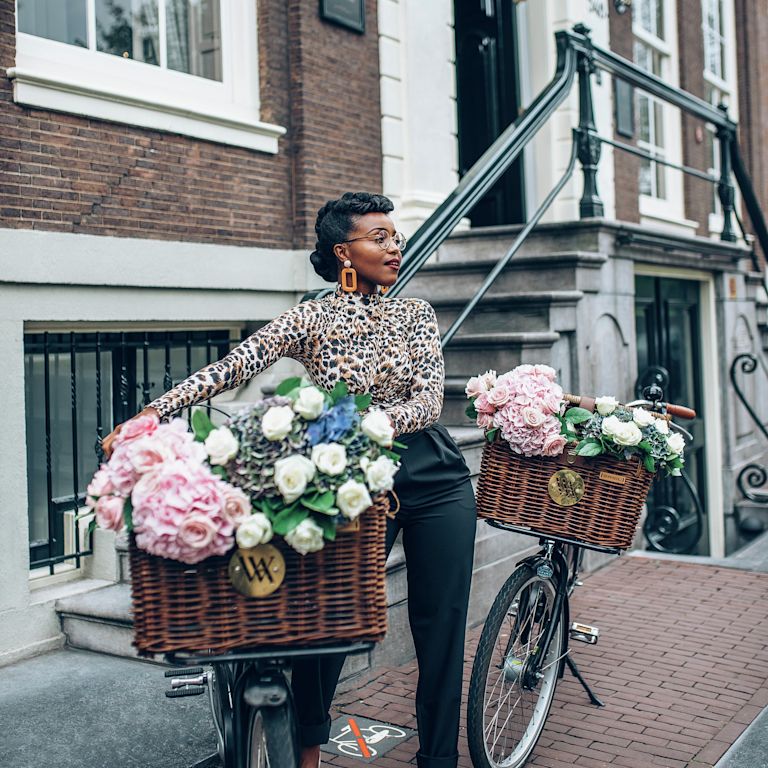 Donna in posa con una bicicletta e un cesto pieno di fiori