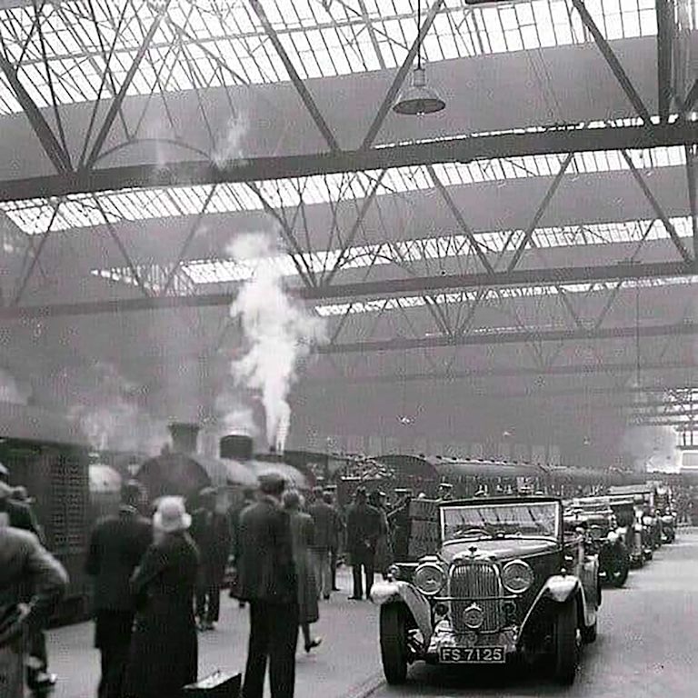 Old shot of people waiting with old cars lined up in black and white