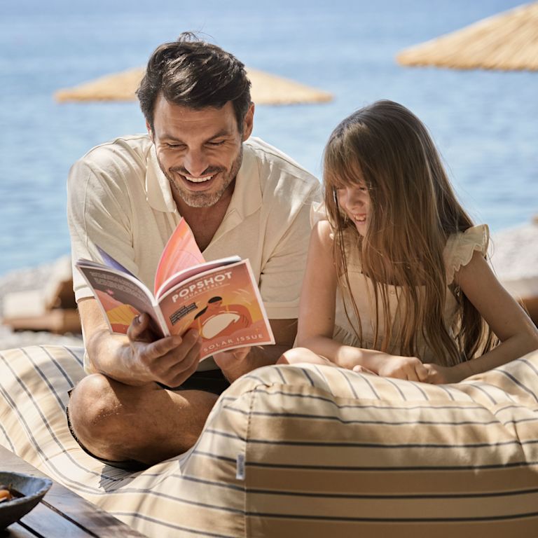 Father and Daughter Reading a Book and Snacking on Fruits at the Beach
