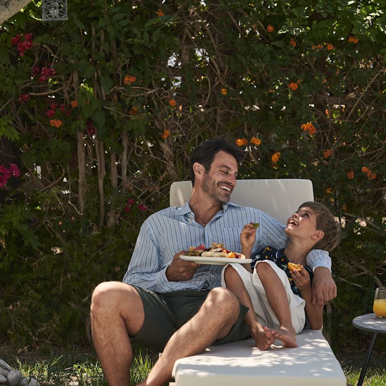 Man and Son Lying on a Lounge Chair, Laughing and Snacking