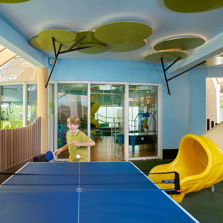 Boy playing ping pong in a covered game room.