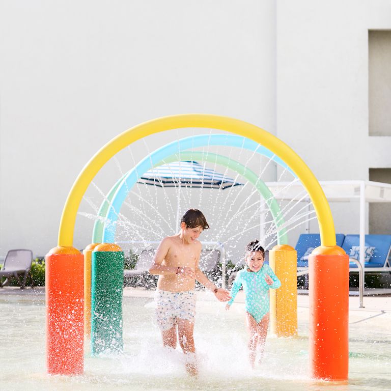 Brother and sister playing in sprinklers at water park.