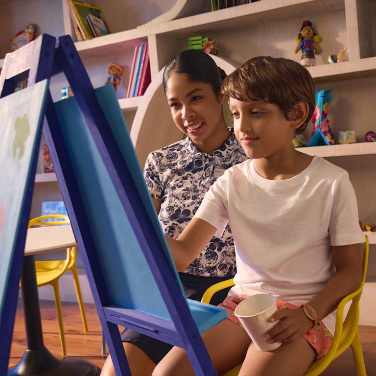 Un garçon dessine dans le club pour enfants tandis qu'un membre de l'équipe le regarde dessiner