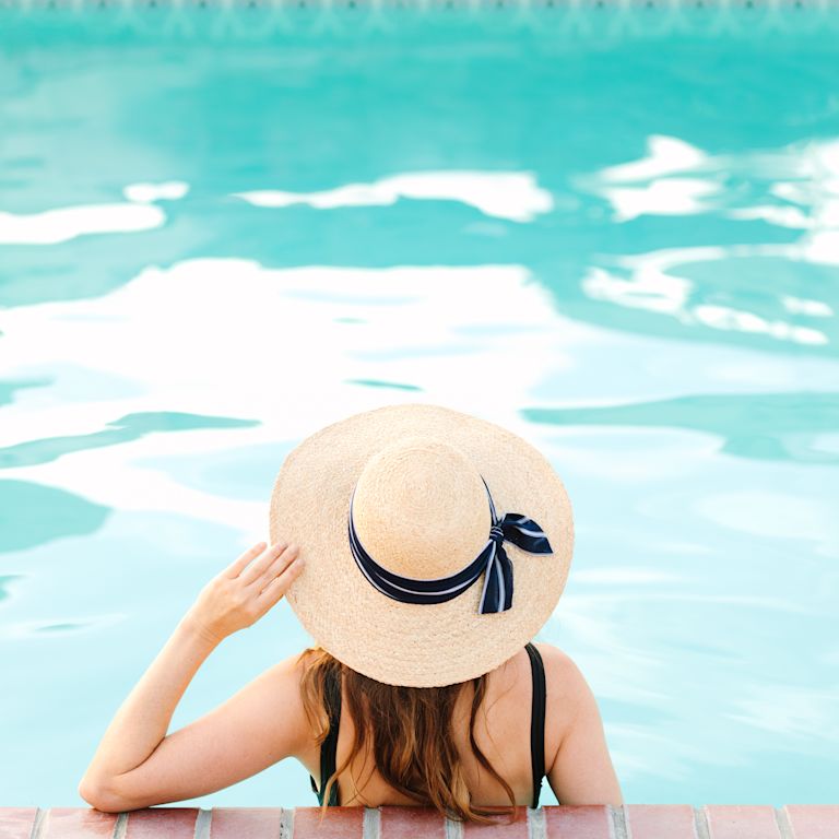 Woman in pool, with hand on hat