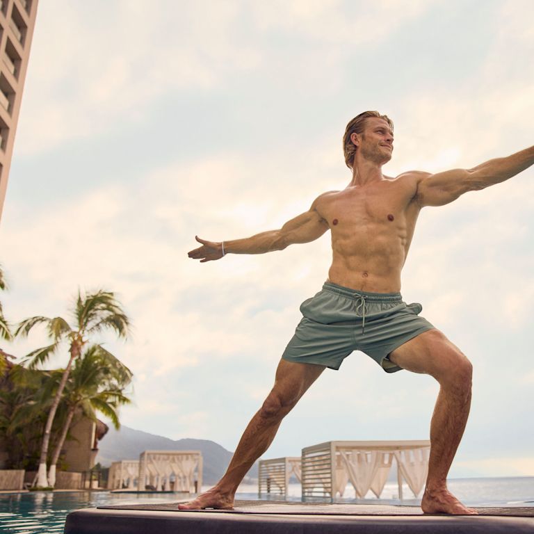 Bărbat care practică yoga în echilibru pe o planșă plutitoare din piscină