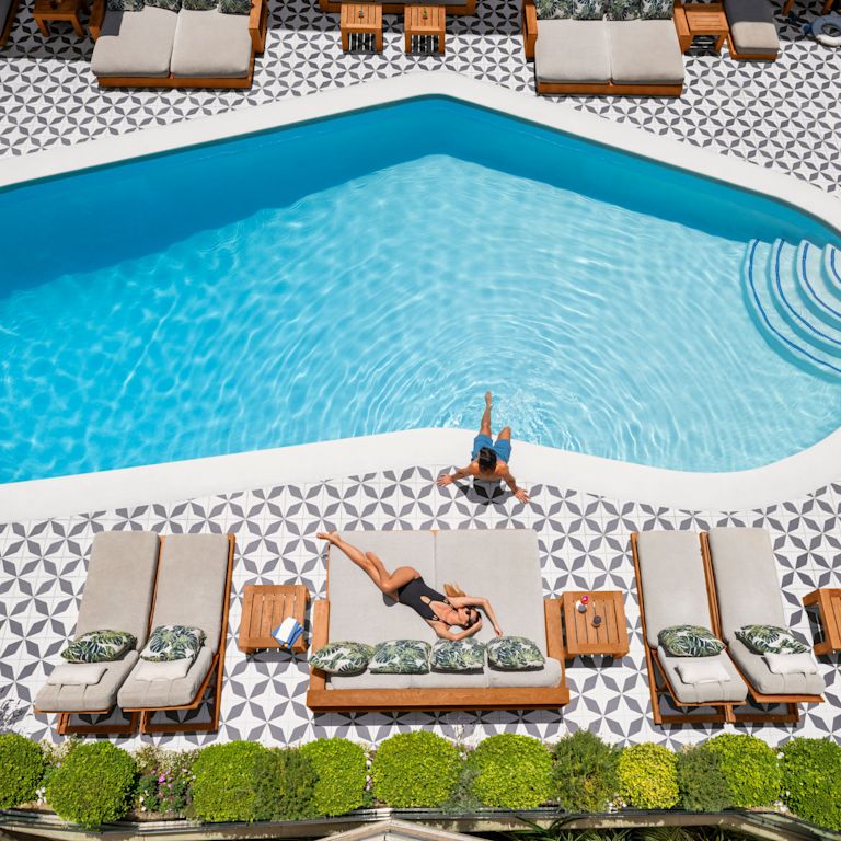 Foto aérea ampla de uma mulher tomando sol na piscina com um homem sentado na piscina