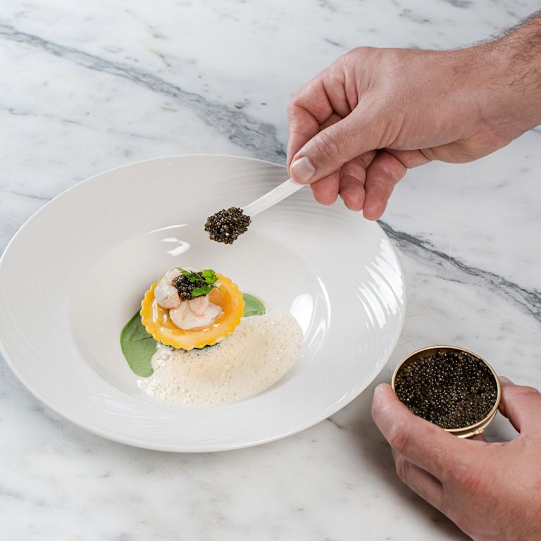 Persona che aggiunge gli ultimi tocchi a un piatto al ristorante Gordon Ramsay au Trianon