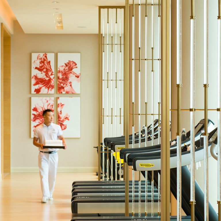 Details of fitness center with treadmills and hotel staff member walking alongside machines