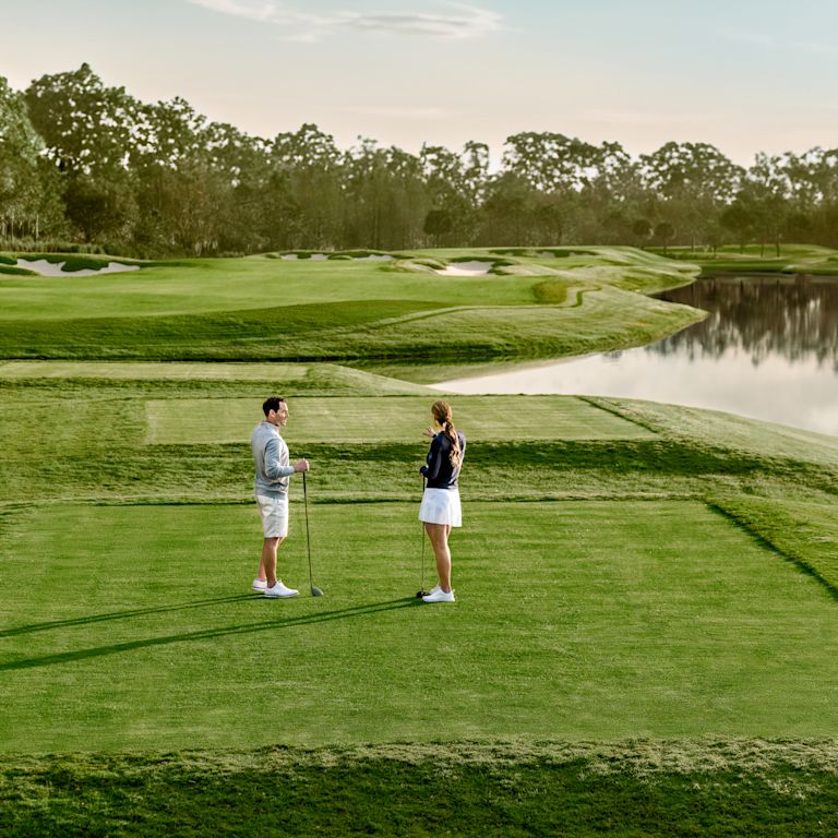 Hombre y mujer de pie en un campo de golf con peligro de agua y árboles
