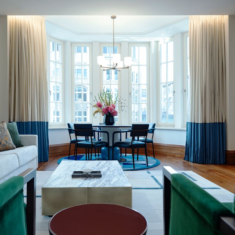 พื้นที่นั่งเล่นในห้องสวีทสําหรับแขก โซฟา โต๊ะกาแฟ เก้าอี้ โต๊ะรับประทานอาหาร วิวหน้าต่างของเมือง