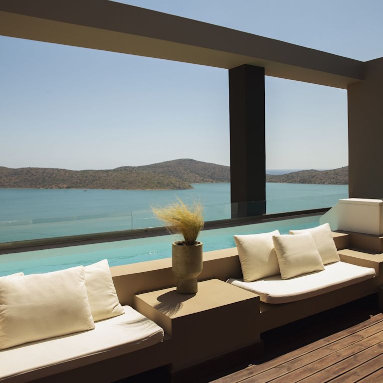 Salotto esterno con accesso condiviso alla piscina, panche bianche imbottite e vista sull'oceano e sulle montagne.