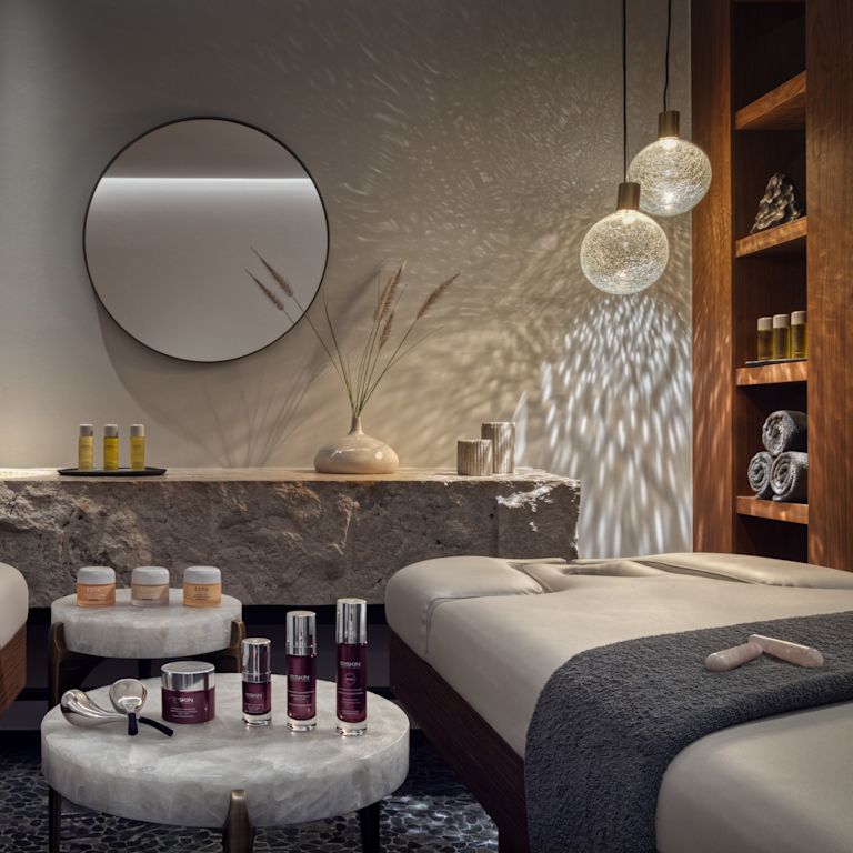 Spa treatment room with two massage beds and products on a round table.