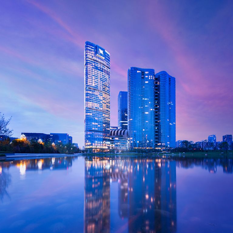 Hotel exterior view lit up at dusk, across body of water