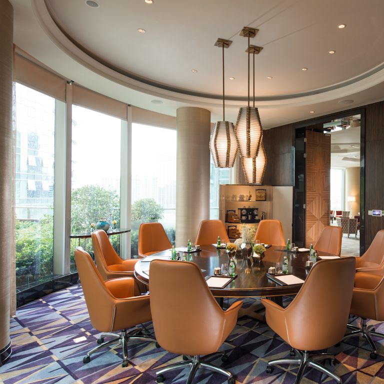 Boardroom with large round table, chairs, TV, and floor-to-ceiling windows with outdoor view