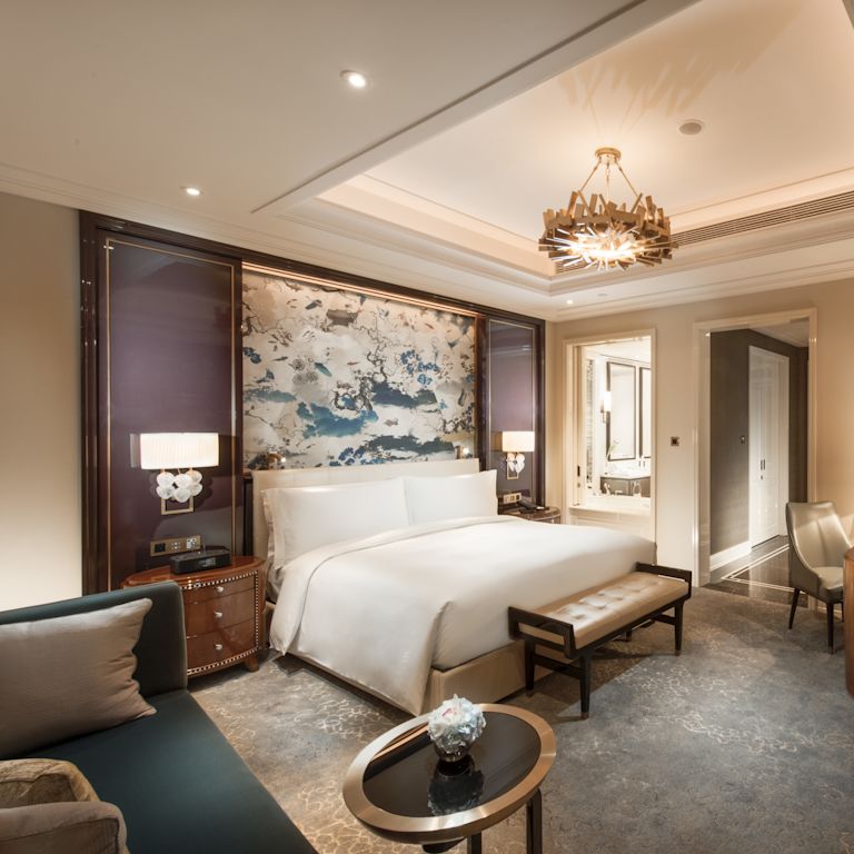 Deluxe room with king bed, footrest, lounge sofa, work desk, and large art displayed above bed