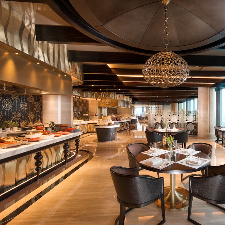 Brasserie 99 dining area with buffet serving station, dining tables with chairs, and floor-to-ceiling windows with outdoor view