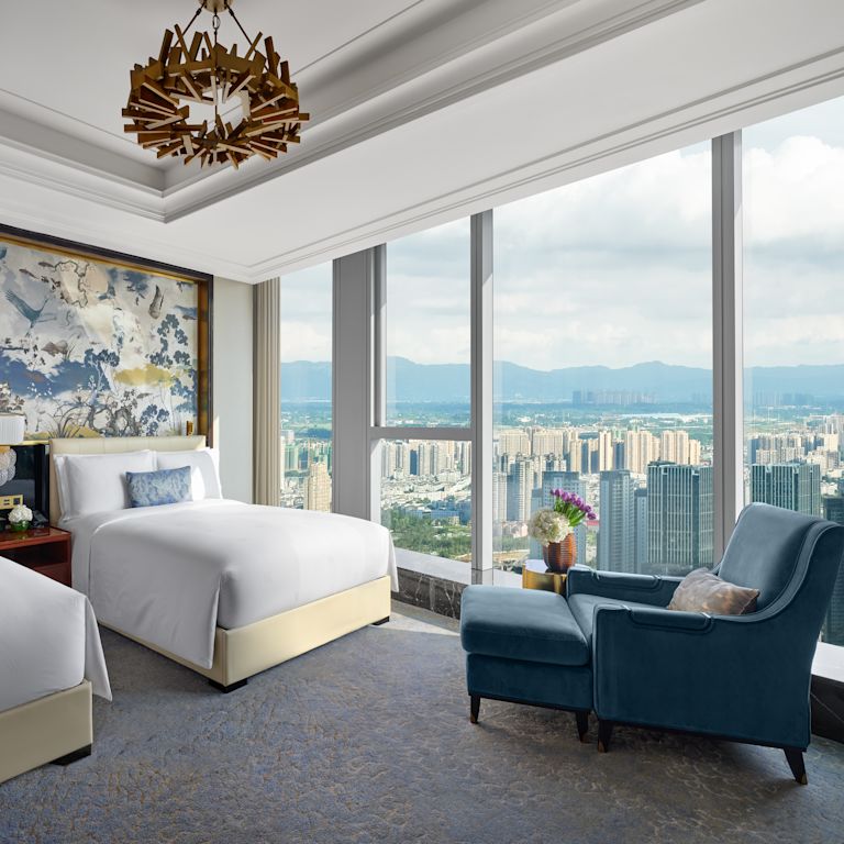guest room, two beds, lounge chair, window view of the city