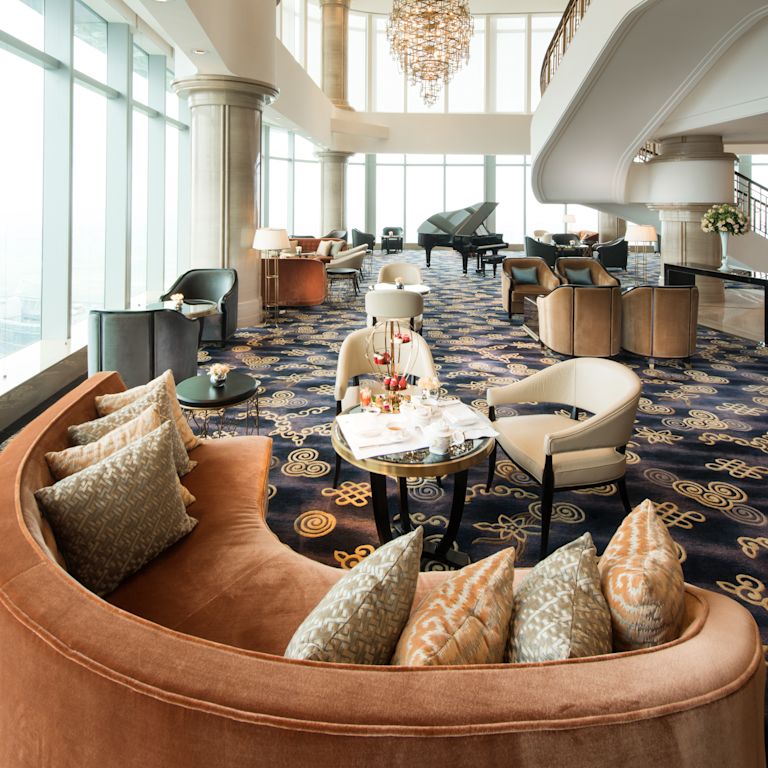 Peacock Alley lounge with curved sofas, soft chairs, coffee tables, piano, and large floor-to-ceiling windows with outdoor view