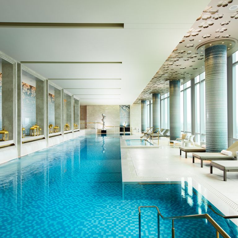 Lavish indoor pool with lounge chairs and floor-to-ceiling windows with outdoor view