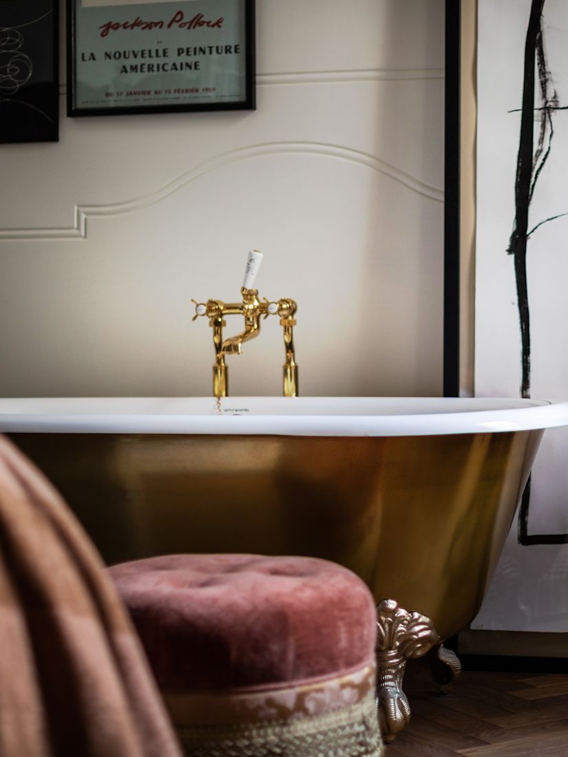 Bathroom with stand-alone gold bathtub, pink velvet chair, and side table holding a fruit plate.-next-transition