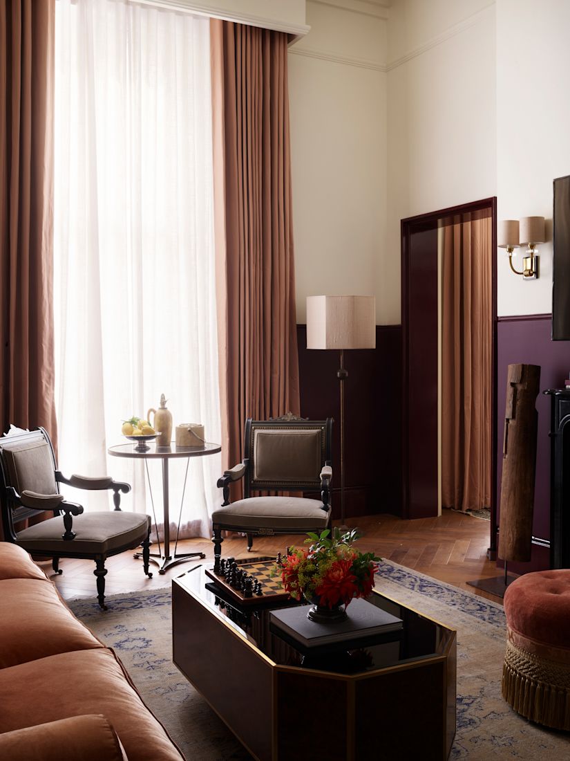 Guest suite light-filled living space with small wooden table, two beige chairs, and a a coffee table with chess.-previous-transition