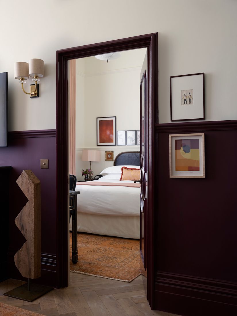 View through a doorway to a bedroom with a bed, framed art on walls, and dark wood paneling.-next-transition