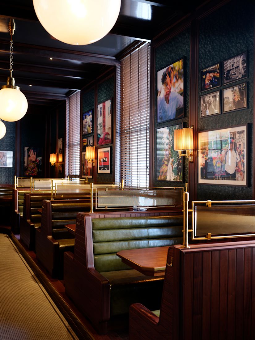 Side Hustle Restaurant green leather booths, dark wood panelling, framed photos on the walls, and globe lights.-previous-transition
