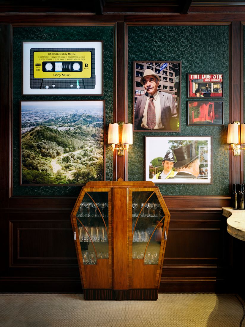 A dark green wall with framed photos, a yellow cassette tape, and a wooden wine cabinet below sconces.-previous-transition