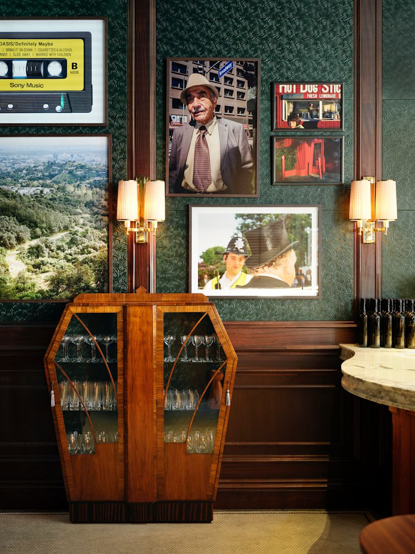 Side Hustle bar with dark green walls, a wooden wine cabinet, framed vintage photos and a yellow cassette tape on the wall.-next-transition