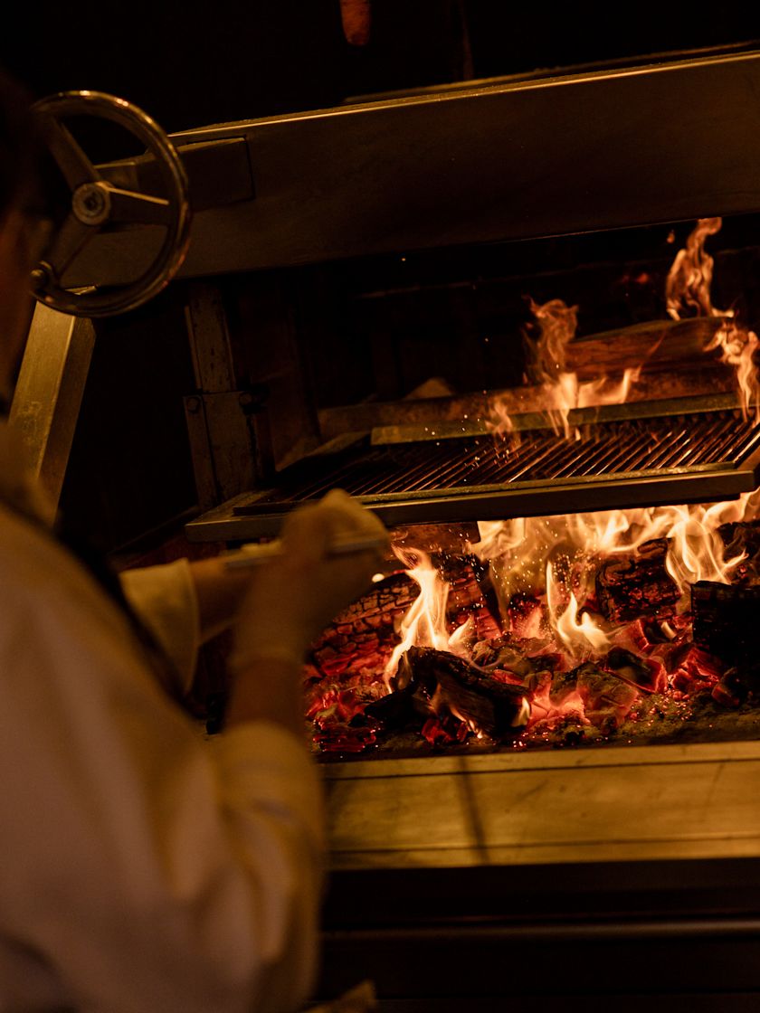 Cook tending a flaming grill with metal racks and glowing coals-next-transition