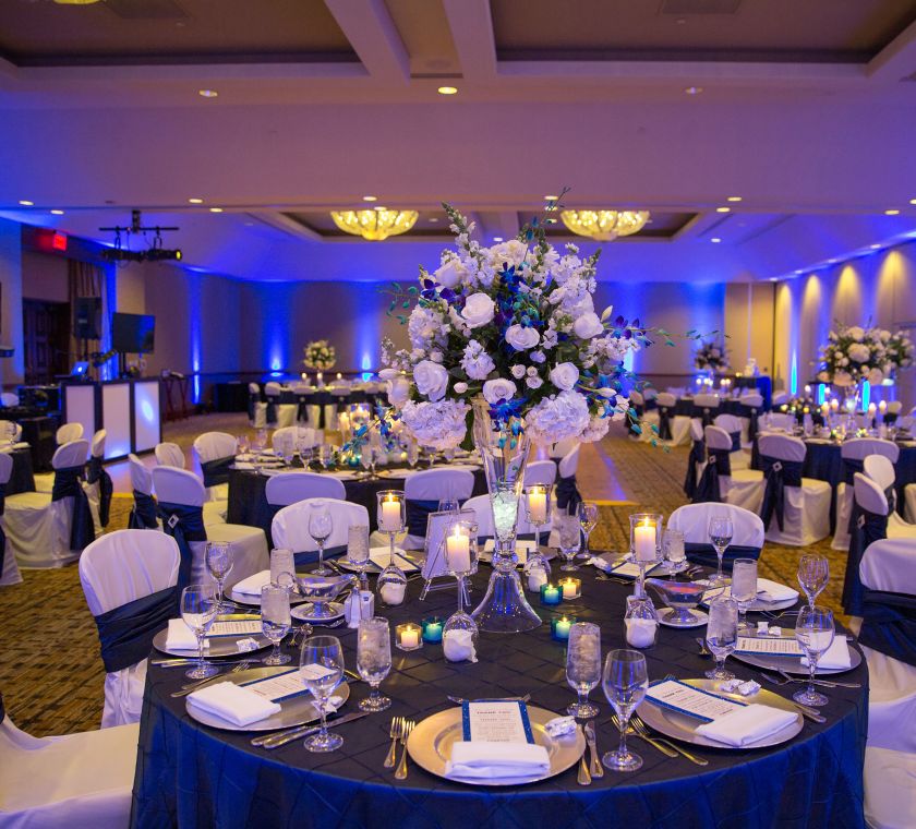 Round tables with blue linens and covered chairs for a wedding reception in the ballroom