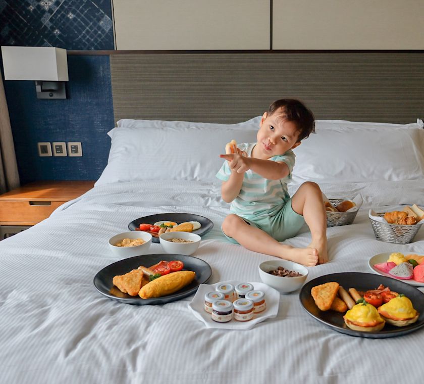 ベッドに腰掛けて料理を片手に座る少年